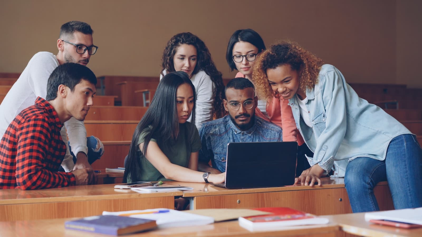 A small group of students gathered around a laptop, talking and pointing at the screen